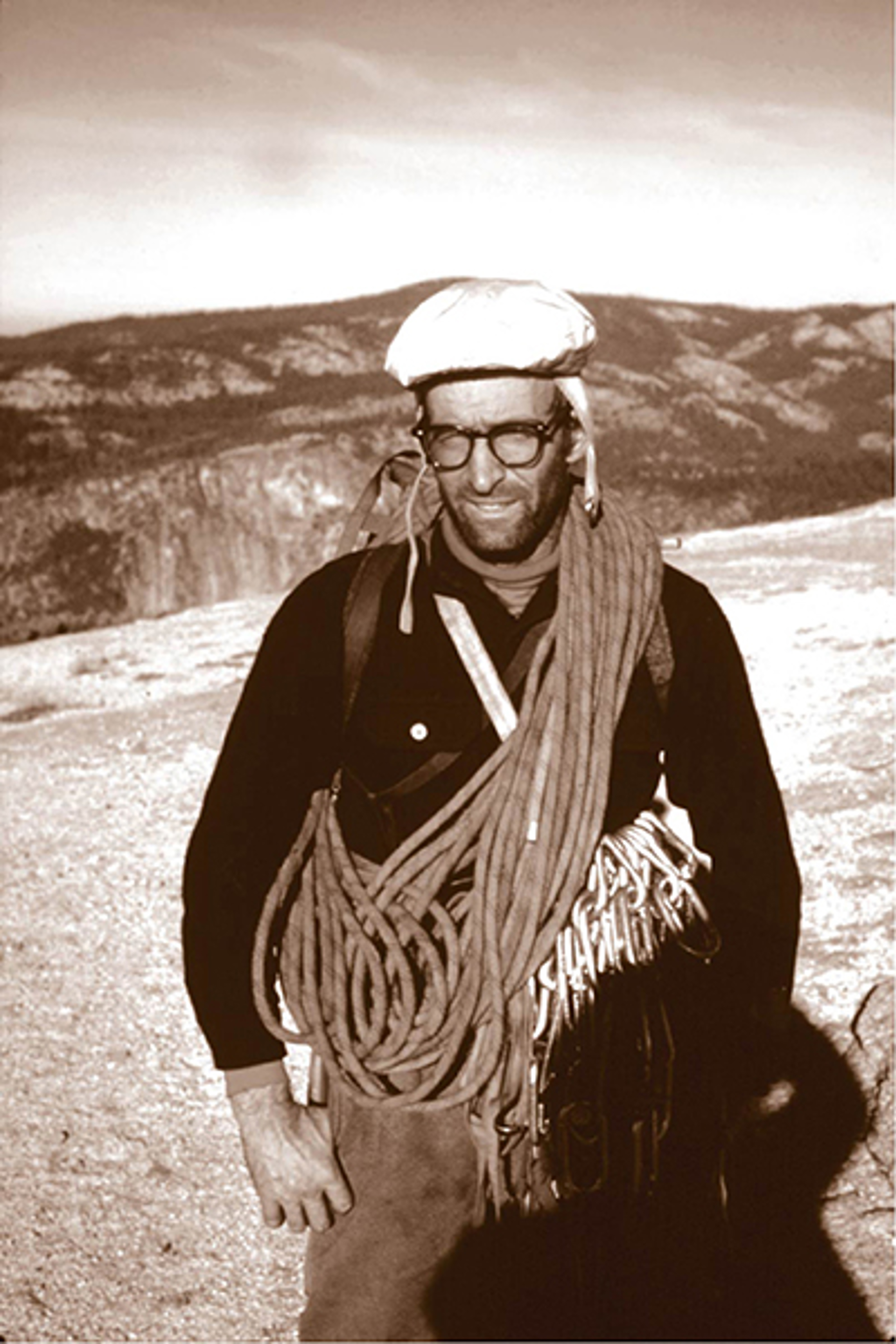 Royal Robbins carrying climbing gear and ropes wearing signature white hat.